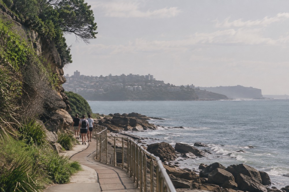 A paved coastal promenade curving along a rocky shoreline with calm water beyond