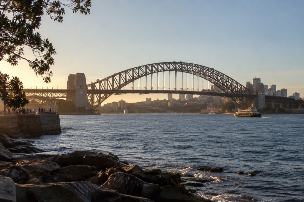 The full steel arch of the bridge seen from the northern shore with the city behind