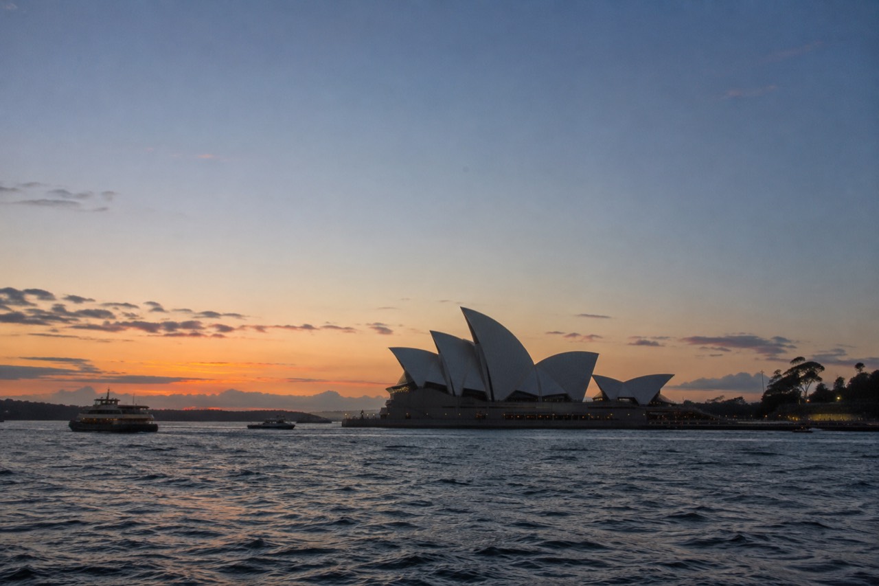 White sail-shaped roofs of the Sydney Opera House against a blue sky above the harbour