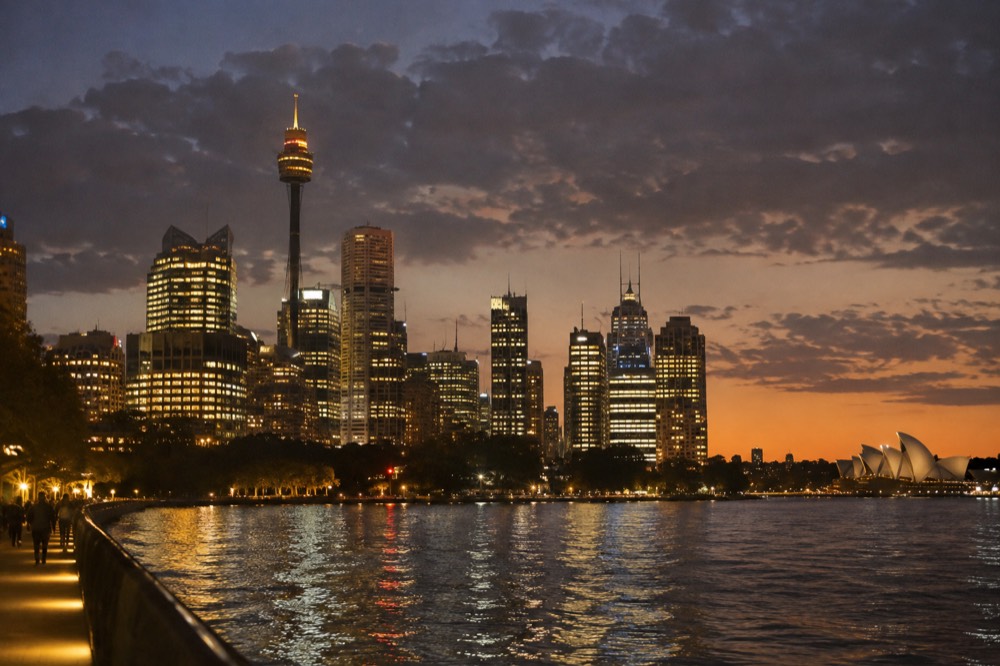 City skyline at dusk with illuminated buildings and harbour water reflecting evening light