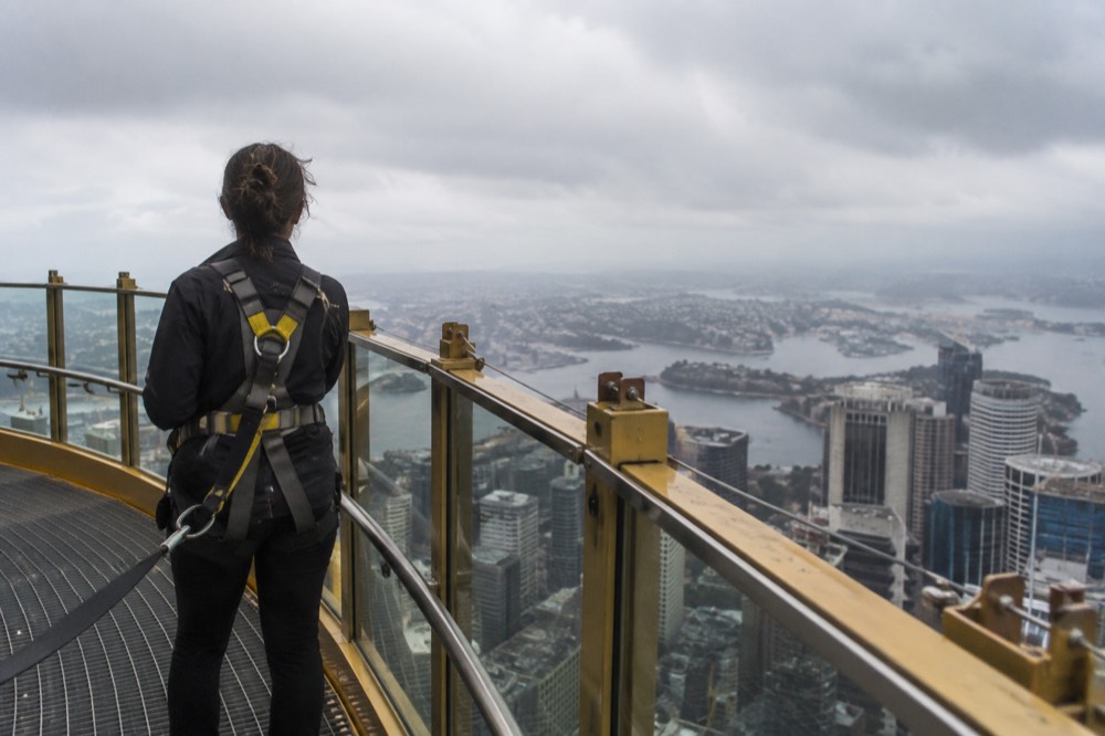 Outdoor walkway at the top of a tall tower with safety harnesses and city views on all sides