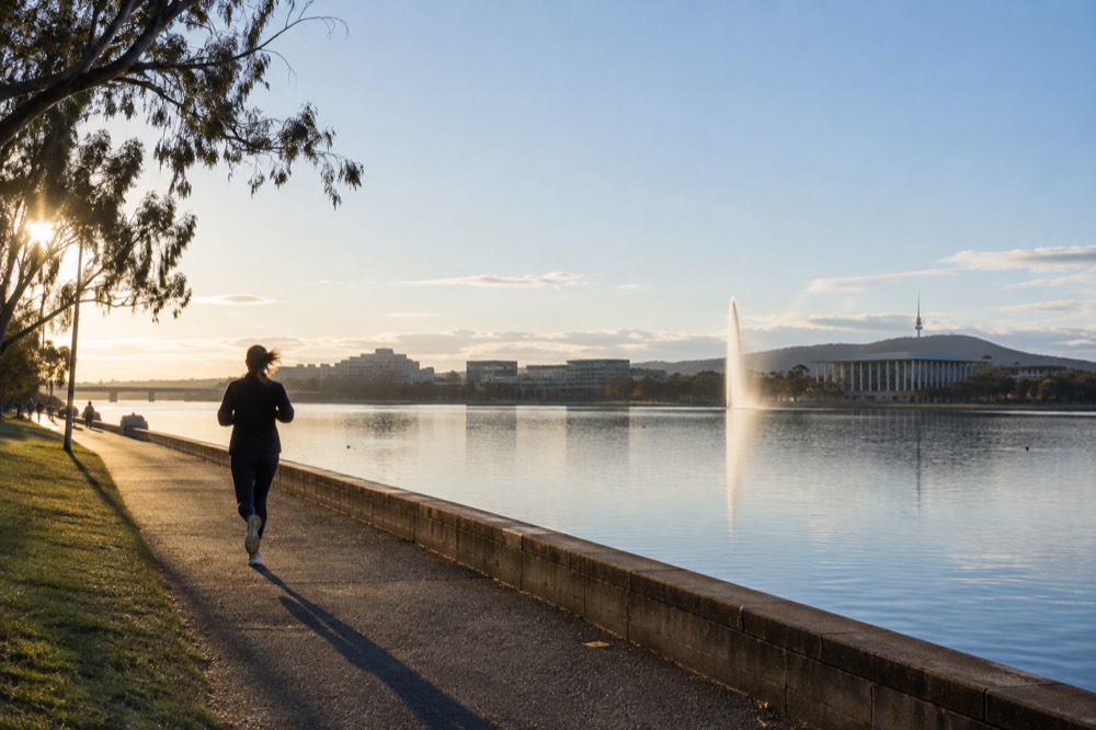 Still lake with a fountain and modern public buildings along the shore under a wide sky