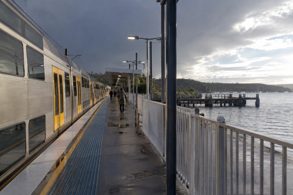 A double-deck train at a station platform beside a water inlet