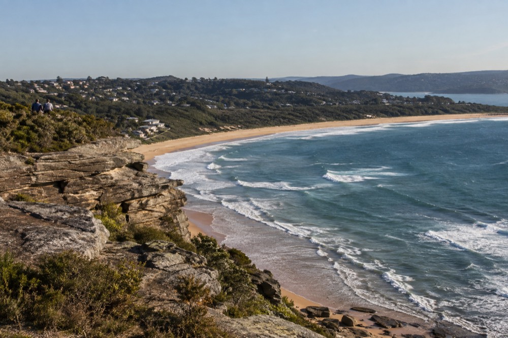 A flat-topped sandstone headland rising above a surf beach at midday