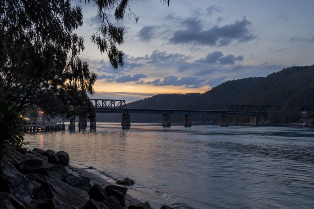 A railway bridge crossing a wide river with bushland hills behind it