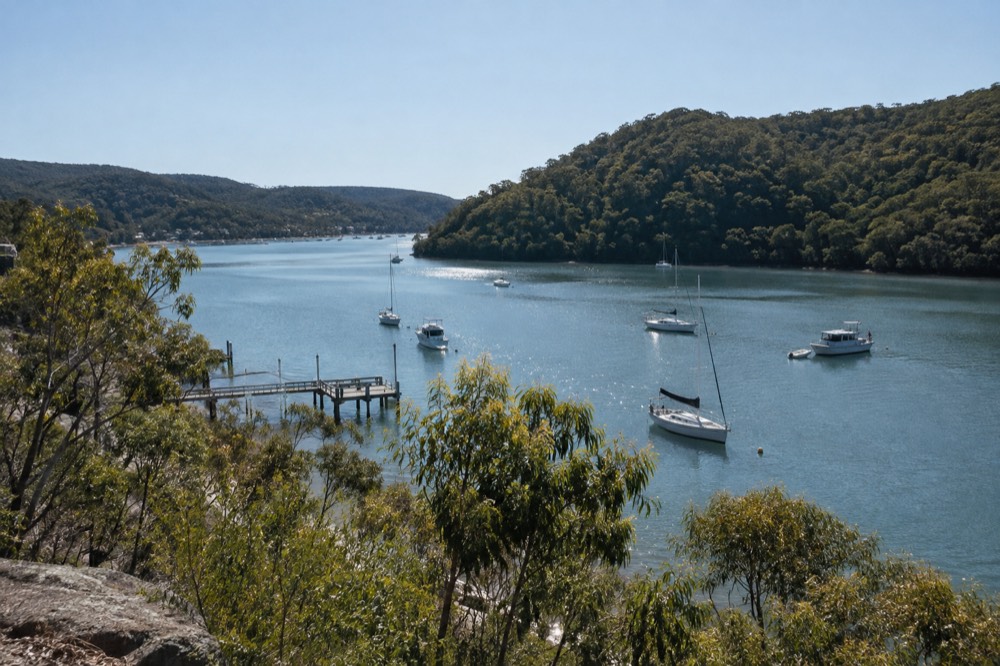 A calm river inlet with moored small boats and tree-covered slopes in morning light