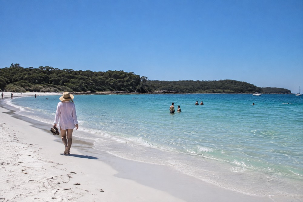 White sand meeting calm turquoise shallows with rounded green headlands behind