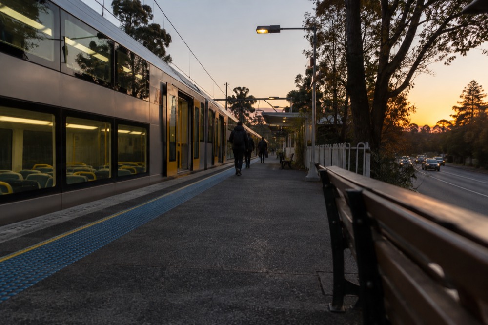 A double-deck train at a mountain station beside a tree-lined street
