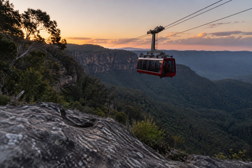 A red cable car moving above a deep forested gorge