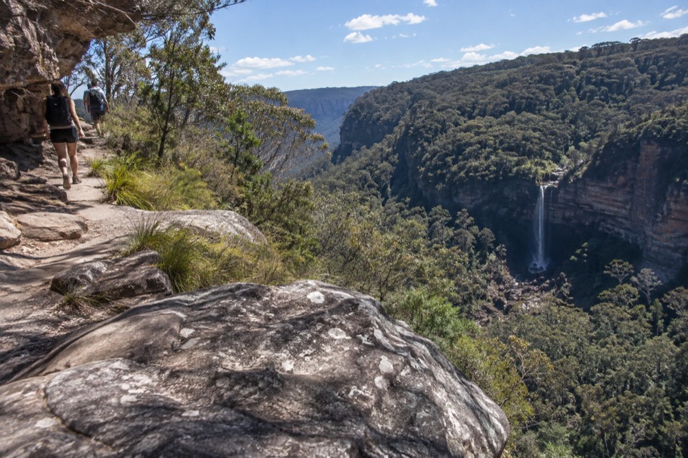 A narrow cliff-top path above a valley with a distant waterfall