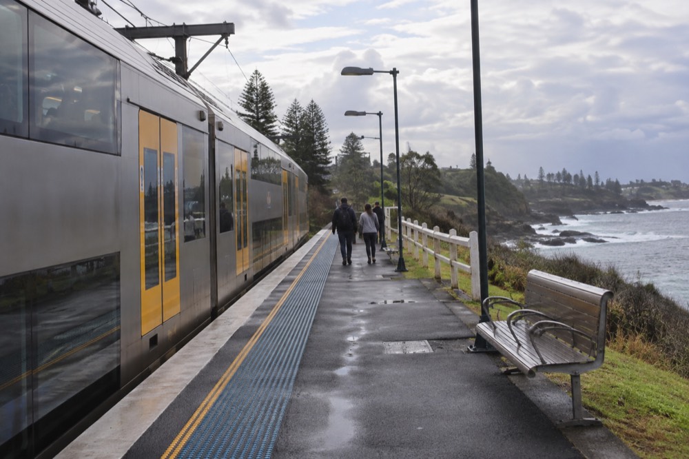 A double-decker train at a small coastal station platform