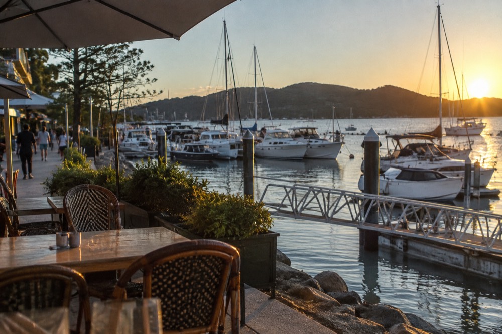 A waterfront cafe strip beside a marina with boats moored in calm water