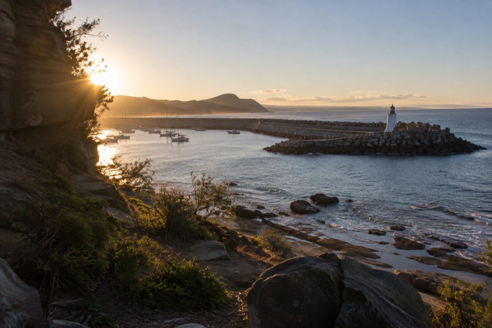 A harbour breakwater with a small lighthouse and boats moored behind