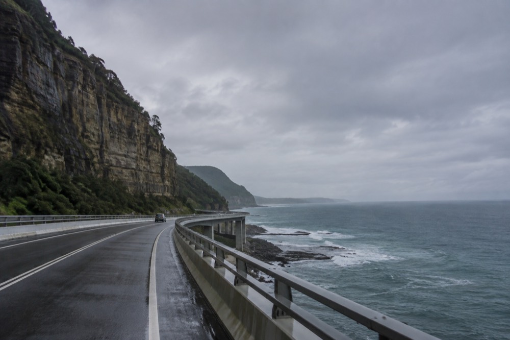 A coastal road winding below an escarpment with ocean horizon beyond