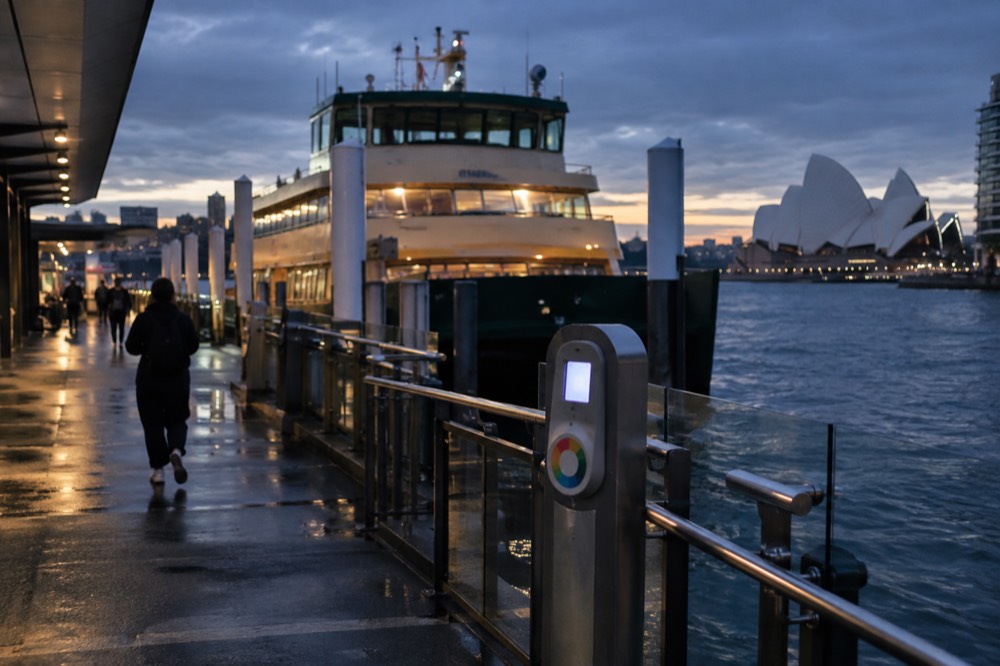 Opal card reader on a ferry wharf with a ferry at the berth behind it