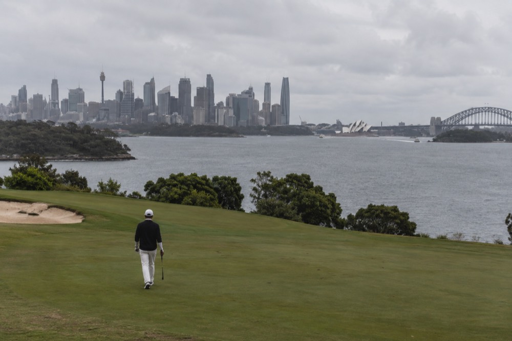 A golfer walking a fairway with the Sydney skyline in the distance