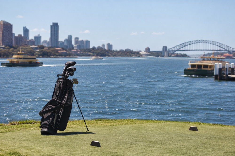 A golf bag resting on a tee box with harbour water in the background