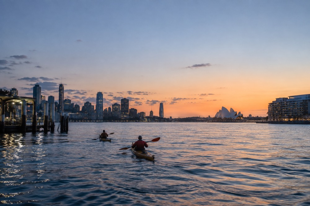 Kayaks on calm harbour water at sunrise with the city behind