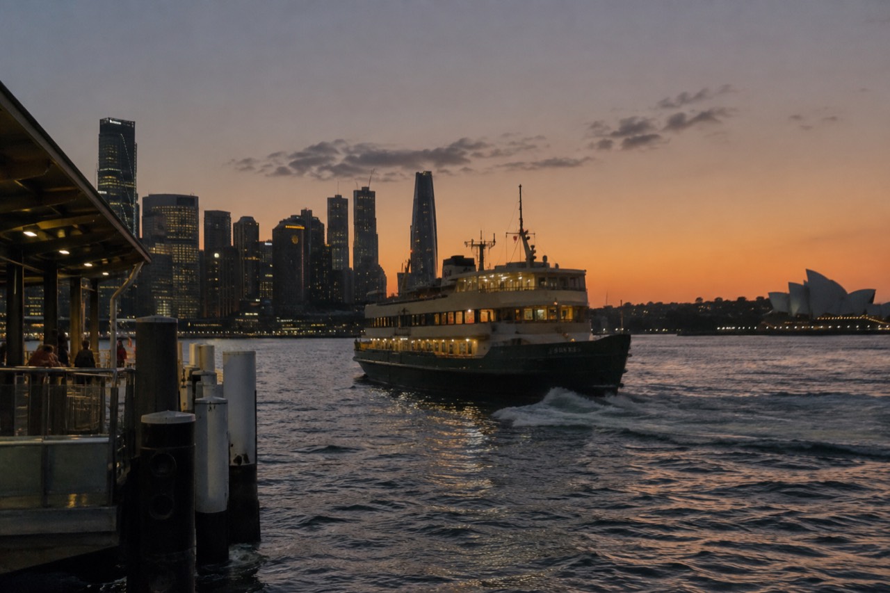 Ferry departing a Sydney wharf at dusk with the city skyline behind it