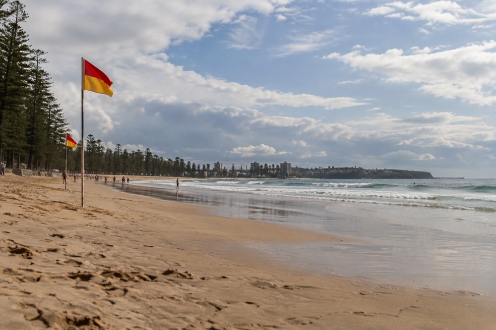 Red and yellow patrol flags on a beach with calm water and lifeguard presence