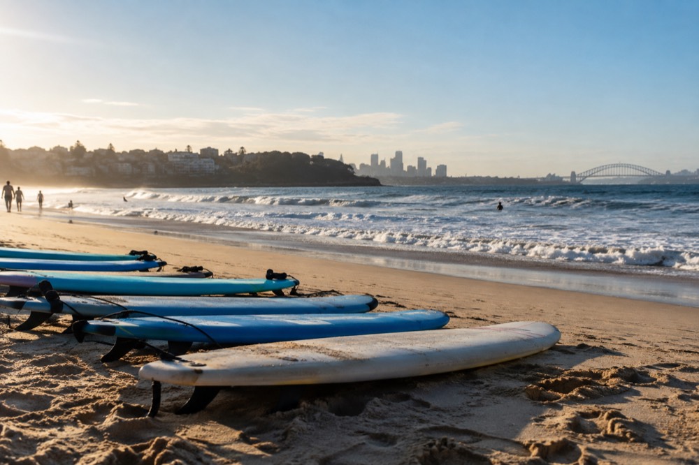 Beginner surfboards lined up on the sand at a wide Sydney beach with rolling waves behind them