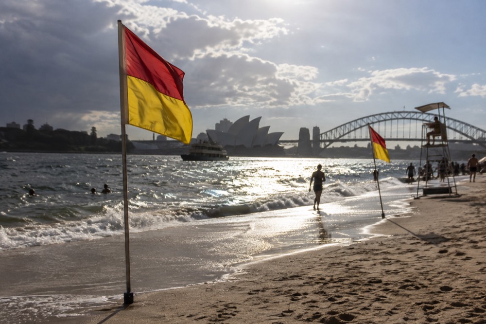 Red and yellow patrol flags planted in smooth wet sand with lifeguard tower in the background