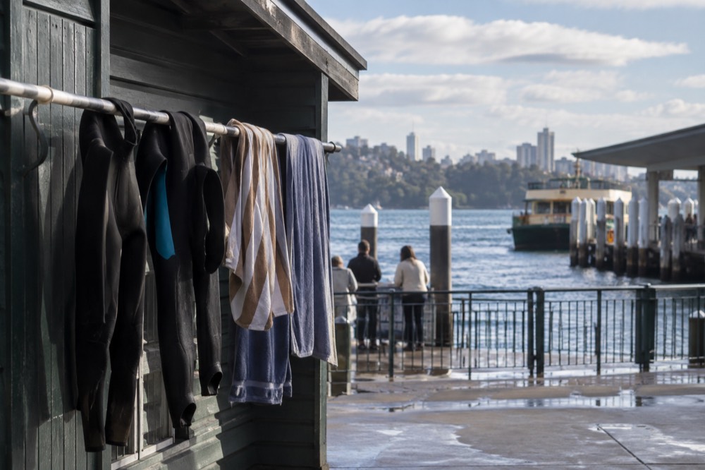 Wetsuits and towels hanging on a rail outside a surf school shed facing the beach