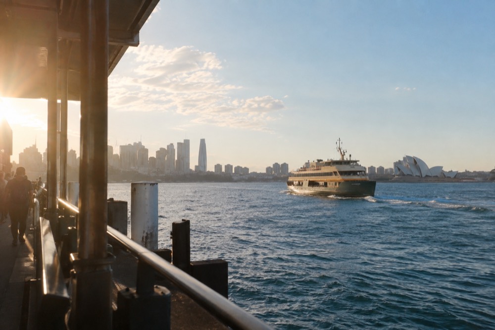 A ferry crossing open harbour water with distant city skyline under a wide sky