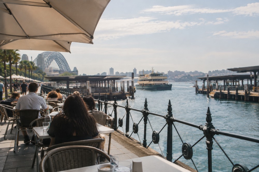 A café strip near a harbour beach with ferry wharf in the background