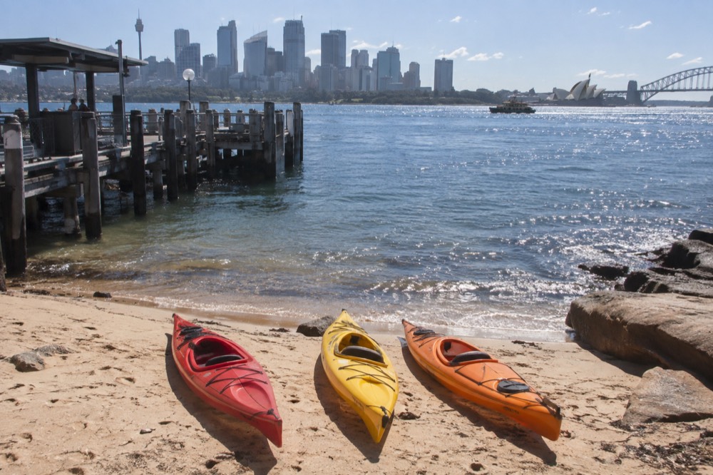 Kayaks resting on a quiet harbour beach with the city skyline across the water