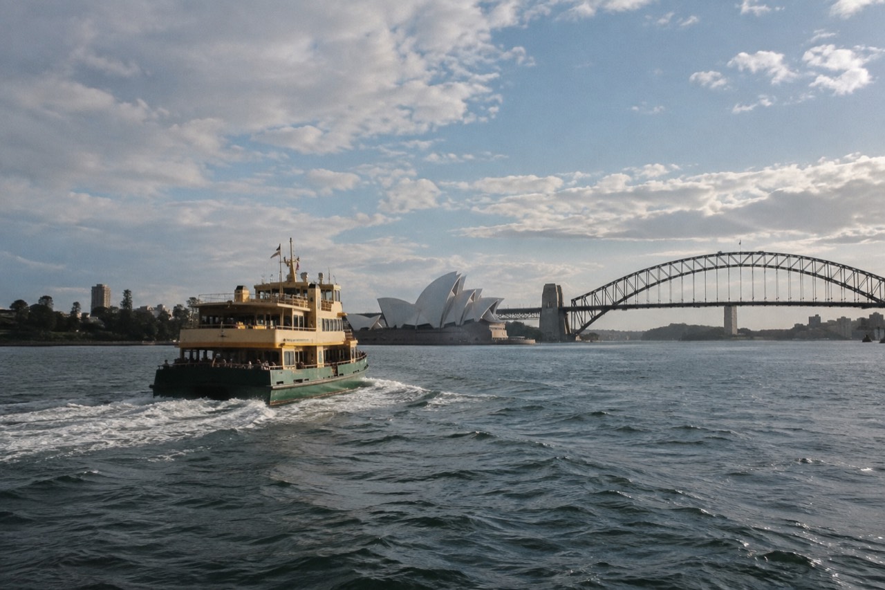 A Sydney ferry crossing the harbour with the Opera House and Harbour Bridge behind it