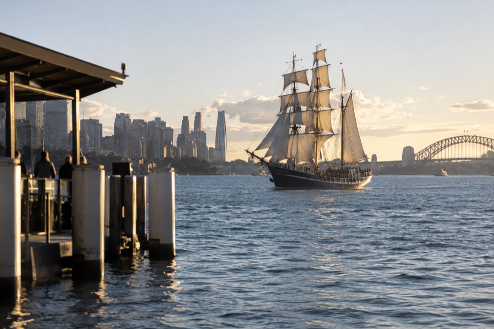 A tall ship with sails raised on Sydney Harbour near the city skyline