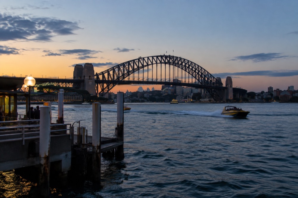 A jet boat carving a wake on Sydney Harbour at sunset with the Harbour Bridge behind