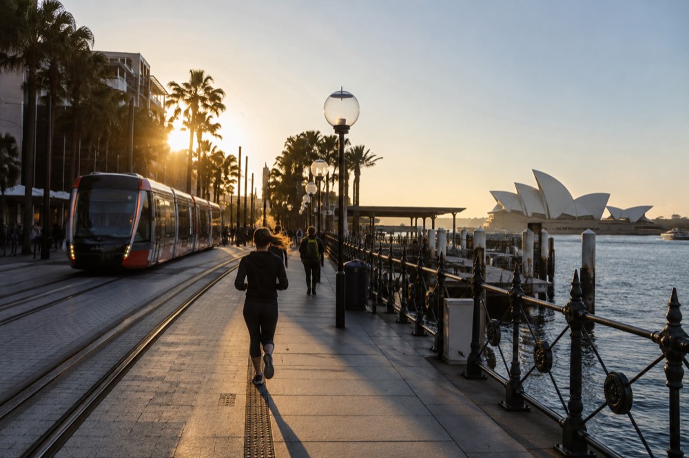 A light rail tram at Circular Quay with the Sydney Opera House visible across the harbour in daylight