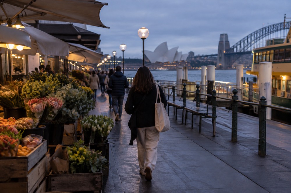 A shopper carrying a cloth bag past flower and produce stalls