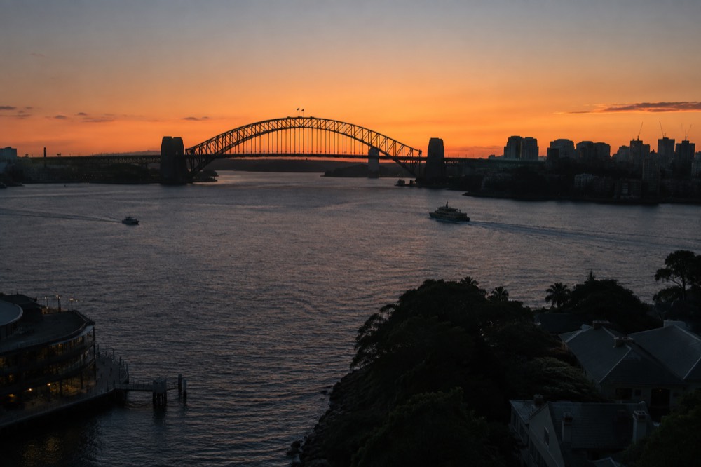 City skyline and Harbour Bridge silhouetted against an orange sunset sky