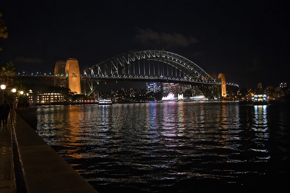 Harbour bridge and city lights reflected in dark water at night