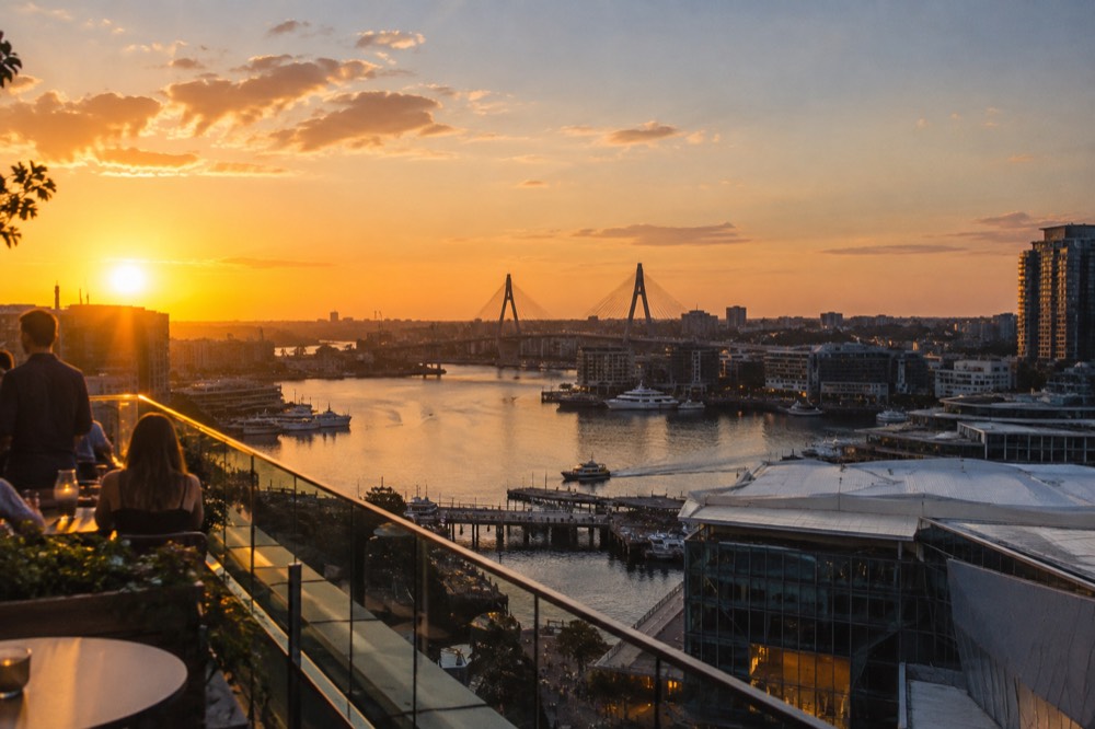 Evening view across Darling Harbour from a high rooftop terrace with the Anzac Bridge in the distance