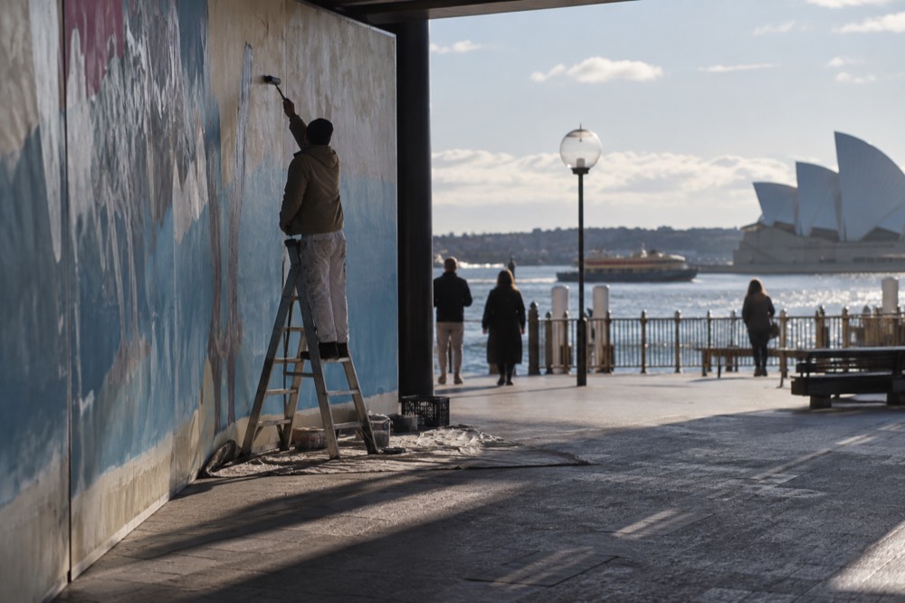 A painter on a ladder working on a large commissioned mural on a shop wall