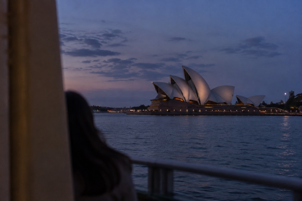 The Sydney Opera House lit at dusk, seen across the water from Circular Quay