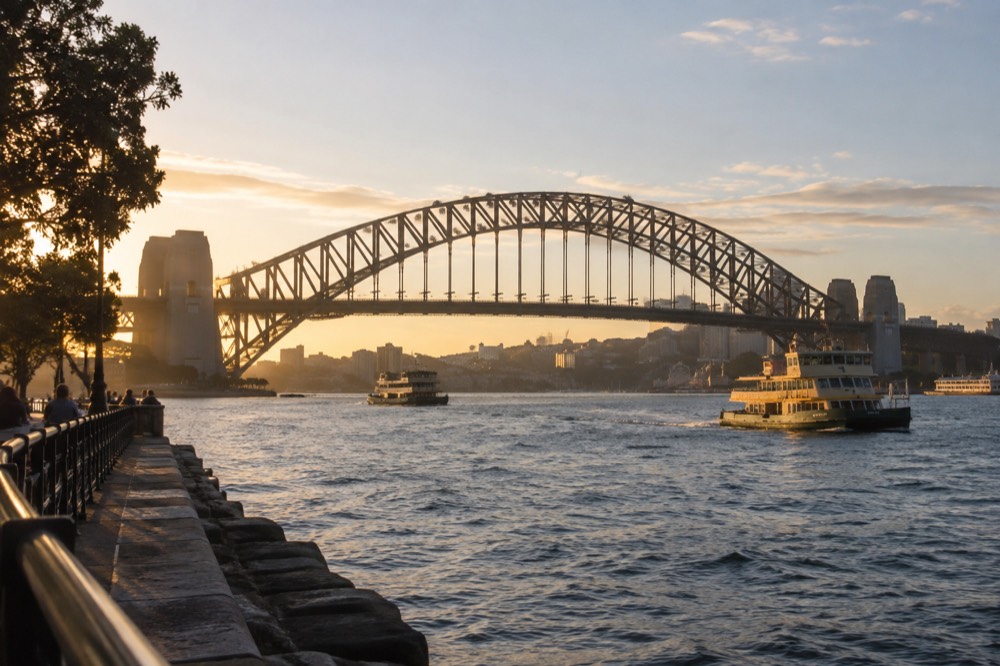 Golden late afternoon light on the Sydney Harbour Bridge and surrounding water with ferries crossing.