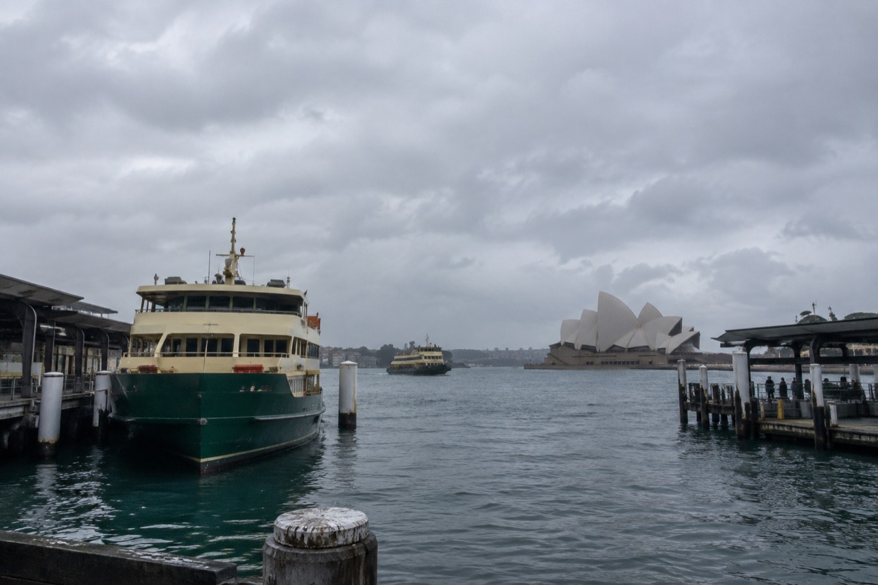 A wide harbour view from Circular Quay with ferries at the wharves and the Opera House in the distance