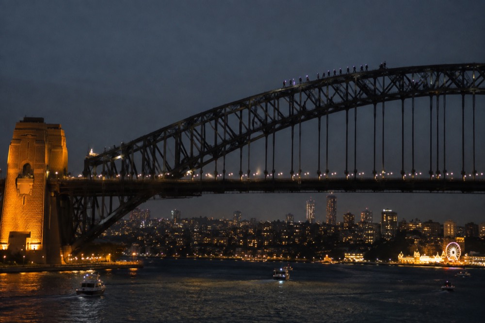 Climbers in suits and headlamps on the upper arch of the Sydney Harbour Bridge at night with the city lit below