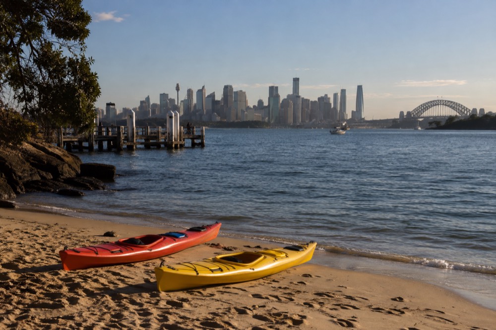 Kayaks resting on a quiet harbour beach with the city skyline in soft morning light