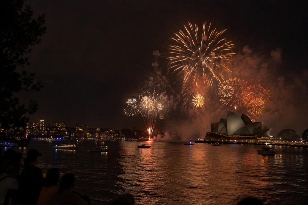 Fireworks bursting over Sydney Harbour with the Opera House silhouetted against the night sky