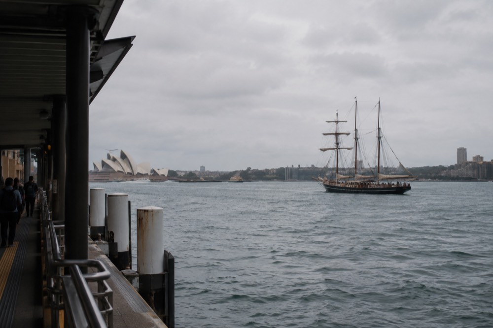 A tall sailing ship with masts and furled sails on open harbour water
