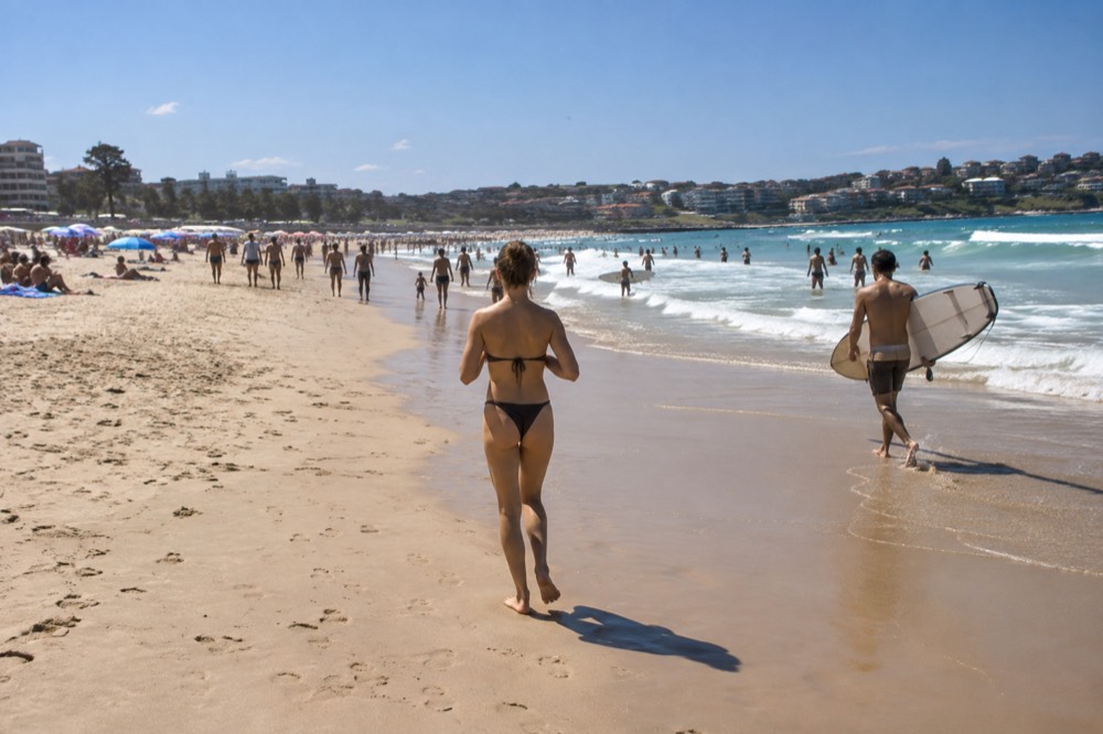 Crowded Bondi Beach with umbrellas and surfers on a bright summer day