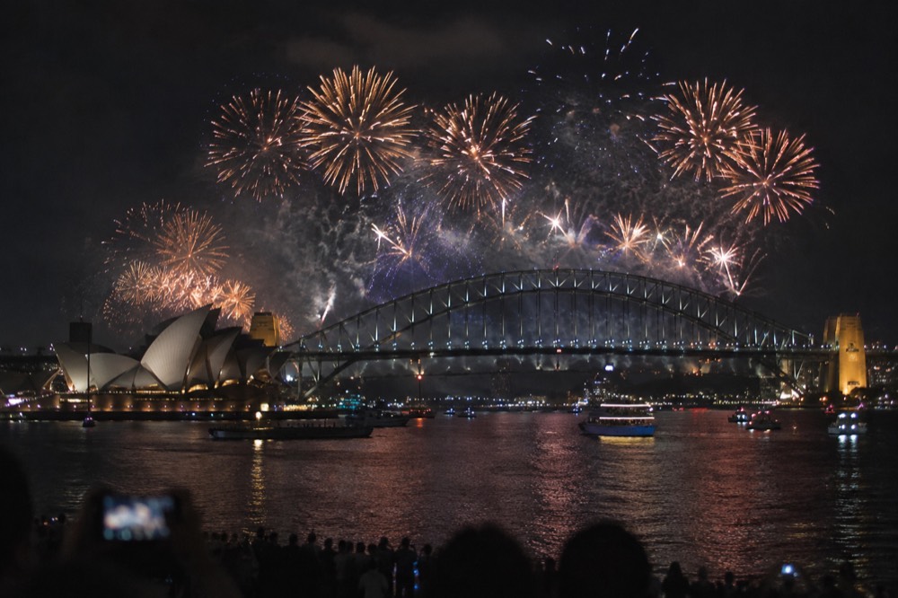 Fireworks bursting over the Sydney Harbour Bridge at midnight with the Opera House silhouetted below