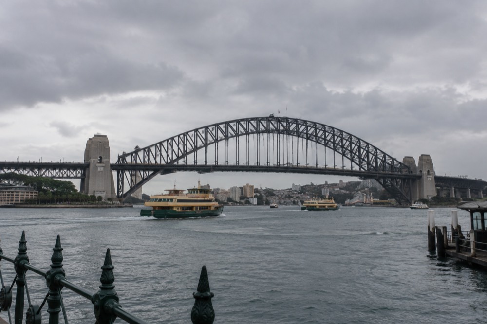 Commuter ferries and a train crossing the harbour bridge in late afternoon light