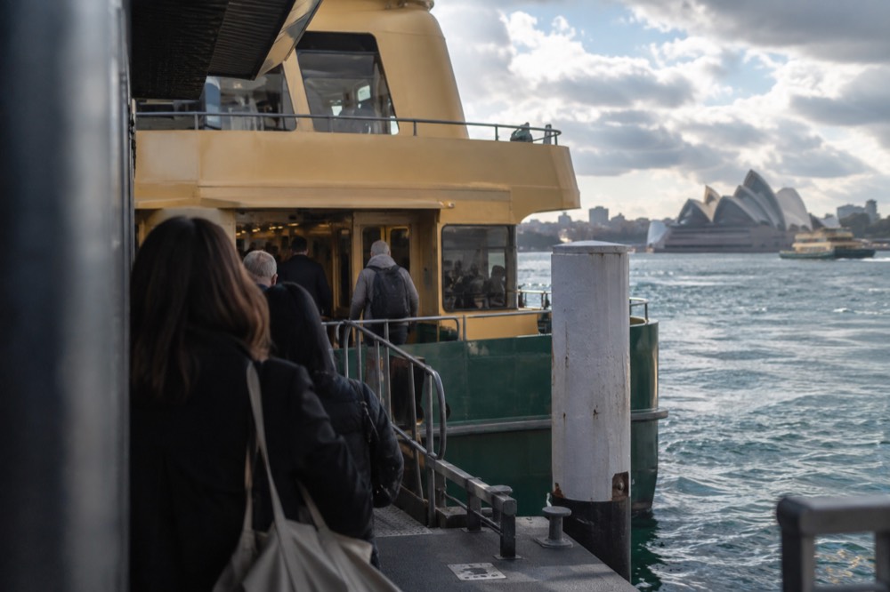 Commuters boarding a green and yellow Sydney ferry at a city wharf